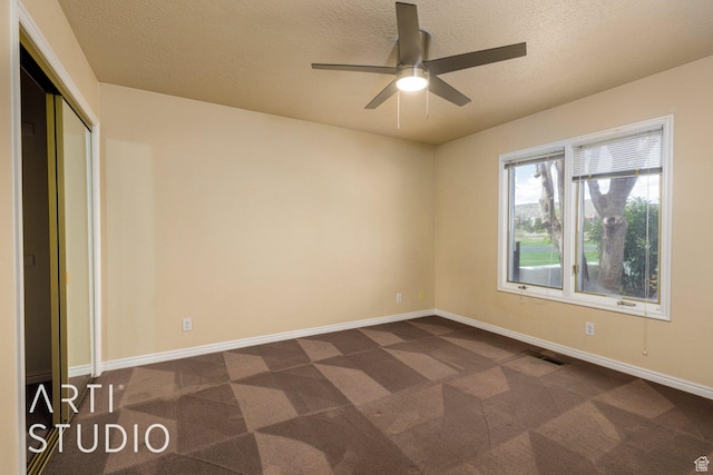 spare room featuring dark carpet, a textured ceiling, a ceiling fan, visible vents, and baseboards