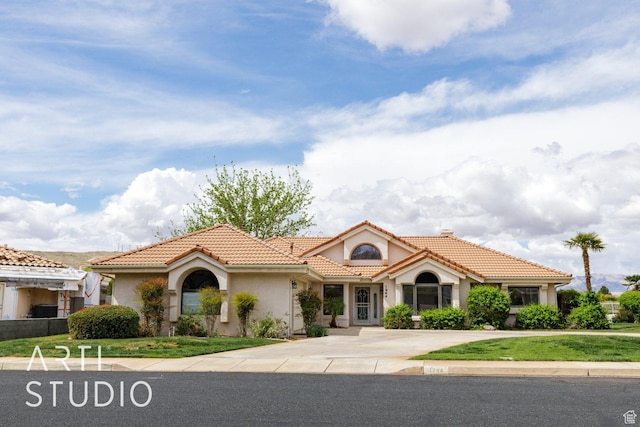 mediterranean / spanish-style home with a tiled roof, concrete driveway, and stucco siding