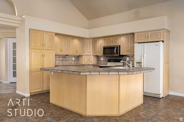 kitchen with range, white refrigerator with ice dispenser, stainless steel microwave, a kitchen island with sink, and tile counters