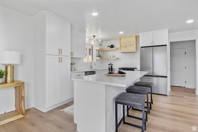 kitchen featuring a kitchen breakfast bar, a kitchen island, appliances with stainless steel finishes, light countertops, and light wood finished floors