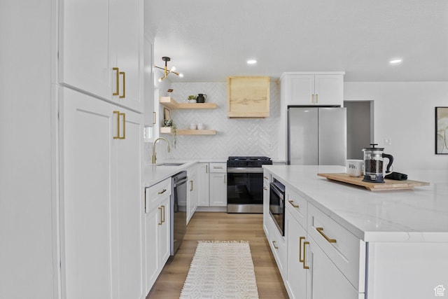 kitchen with light wood-style flooring, tasteful backsplash, white cabinets, appliances with stainless steel finishes, and a sink
