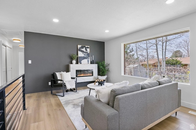 living area with light wood-style floors, a glass covered fireplace, and recessed lighting