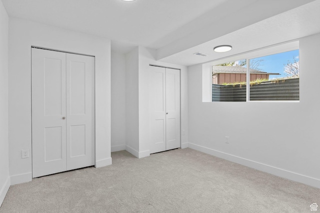 unfurnished bedroom featuring carpet flooring, visible vents, baseboards, and two closets