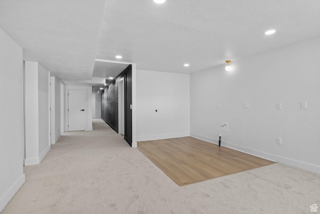finished basement with baseboards, recessed lighting, light carpet, and a textured ceiling