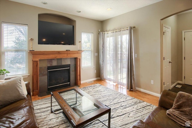 living room with visible vents, baseboards, arched walkways, light wood-type flooring, and a tile fireplace