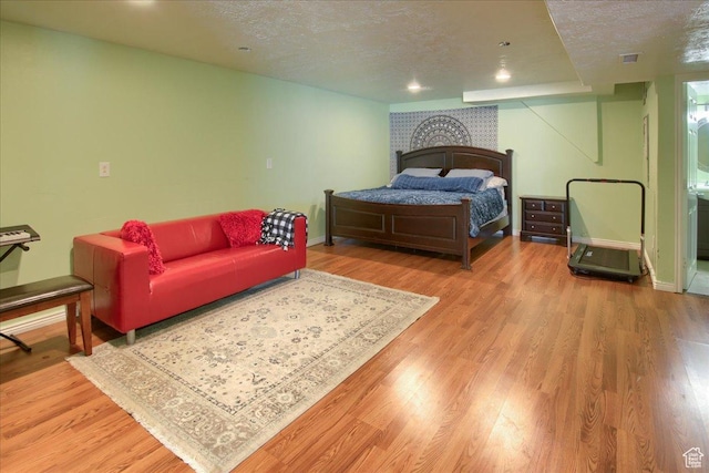 bedroom featuring visible vents, a textured ceiling, baseboards, and wood finished floors
