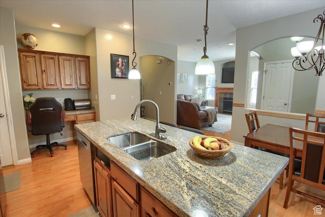 kitchen with decorative light fixtures, a sink, light wood-style floors, light stone countertops, and a tile fireplace