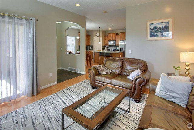 living room featuring baseboards, recessed lighting, visible vents, arched walkways, and light wood finished floors