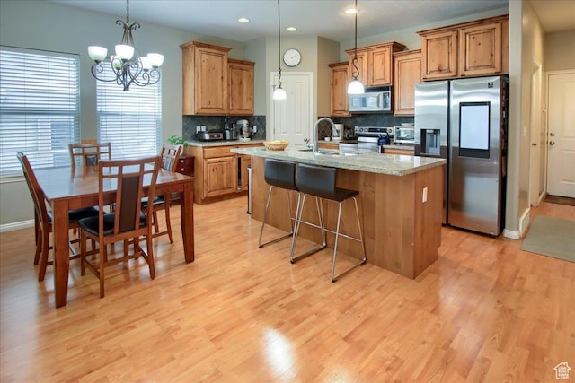 kitchen featuring brown cabinetry, light wood-type flooring, a sink, stainless steel appliances, and a center island with sink