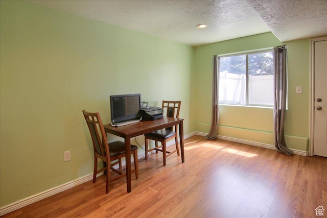 office area featuring baseboards, light wood-type flooring, and a textured ceiling