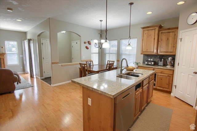 kitchen featuring light wood-type flooring, decorative backsplash, arched walkways, dishwasher, and a sink