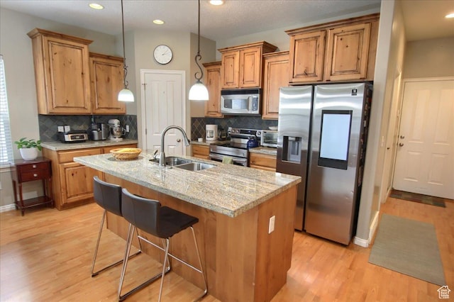 kitchen featuring an island with sink, light wood-style flooring, brown cabinetry, appliances with stainless steel finishes, and a sink