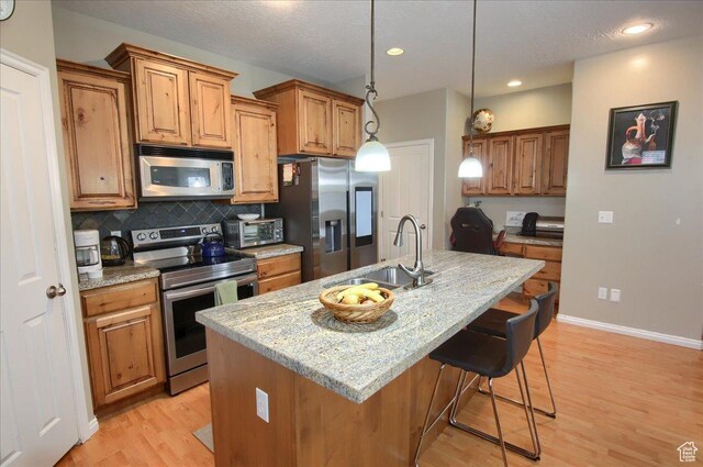 kitchen featuring light wood-style flooring, brown cabinetry, appliances with stainless steel finishes, a sink, and decorative backsplash