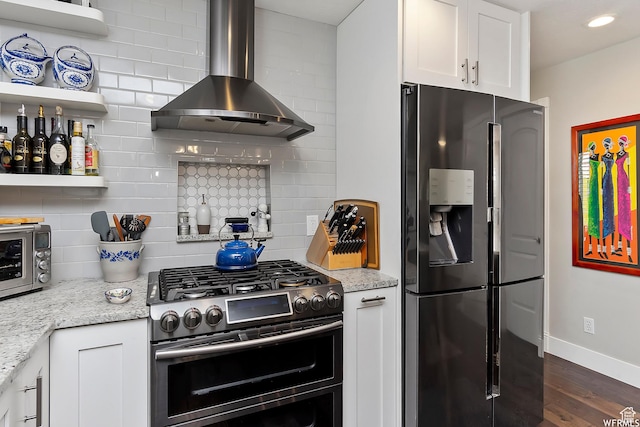 kitchen with appliances with stainless steel finishes, wall chimney exhaust hood, backsplash, and white cabinets