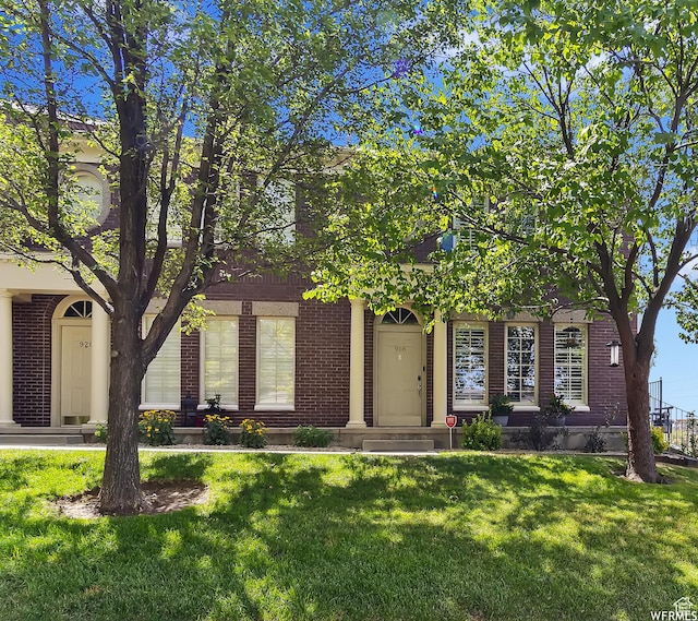 view of property hidden behind natural elements with a front yard and brick siding