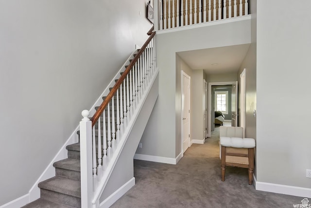 staircase with baseboards, carpet, and a towering ceiling