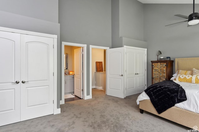 carpeted bedroom featuring a closet, ensuite bathroom, a towering ceiling, and baseboards