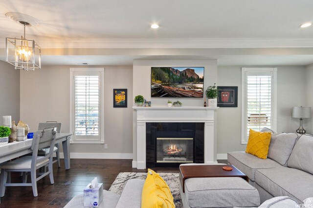 living area featuring baseboards, an inviting chandelier, a tiled fireplace, dark wood finished floors, and crown molding