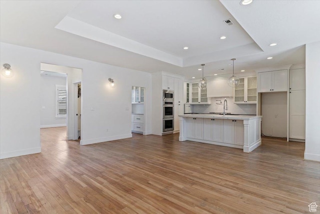 kitchen featuring light wood-style floors, a tray ceiling, white cabinetry, a kitchen island with sink, and open floor plan