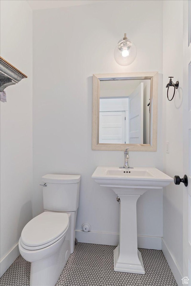 half bathroom featuring toilet, tile patterned floors, a sink, and baseboards