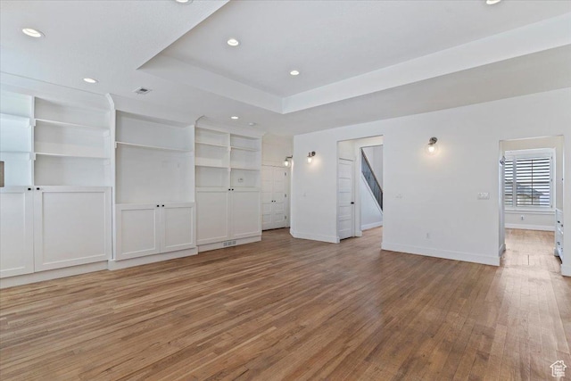 unfurnished living room with a tray ceiling, recessed lighting, baseboards, and light wood-style flooring