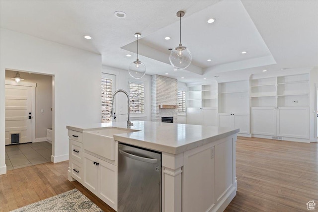 kitchen with a tray ceiling, a large fireplace, dishwasher, a sink, and light wood finished floors