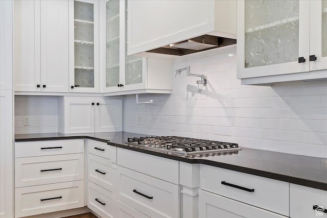 kitchen with stainless steel gas cooktop, decorative backsplash, dark countertops, and white cabinetry