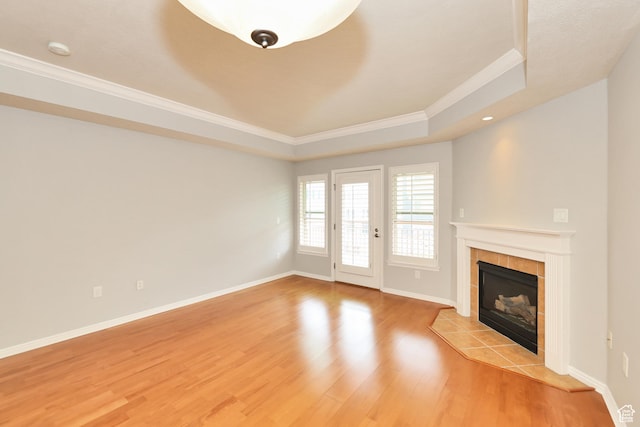 unfurnished living room featuring baseboards, ornamental molding, a fireplace, a tray ceiling, and light wood finished floors