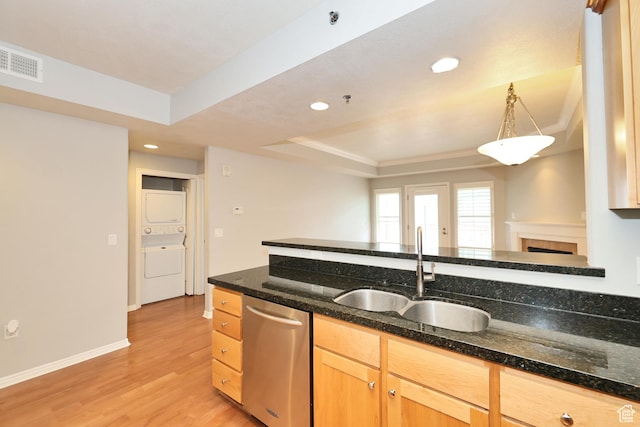 kitchen featuring light wood-type flooring, dishwasher, a sink, a raised ceiling, and stacked washer and clothes dryer
