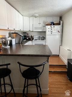 56 E Center St Unit 1, Richfield, UT 84701 - kitchen featuring a peninsula, white appliances, a kitchen bar, and dark countertops