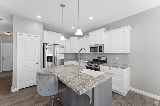 kitchen with white cabinets, dark wood-style flooring, appliances with stainless steel finishes, a center island with sink, and decorative backsplash