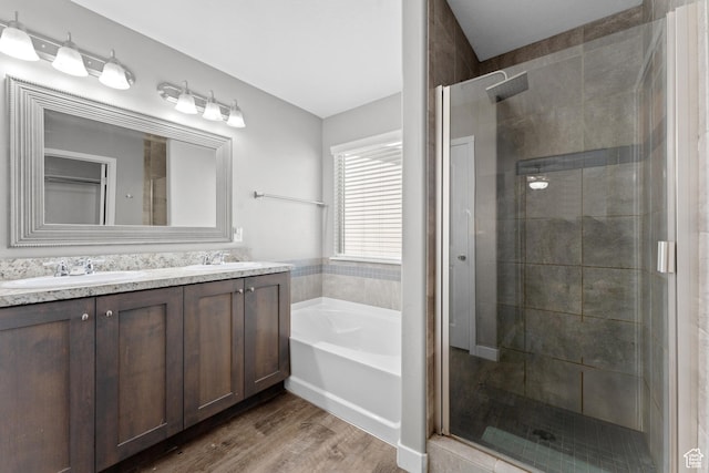 full bath with double vanity, a garden tub, a stall shower, and wood finished floors