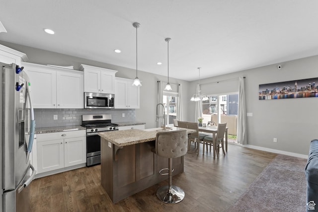 kitchen featuring tasteful backsplash, an island with sink, dark wood finished floors, stainless steel appliances, and a sink
