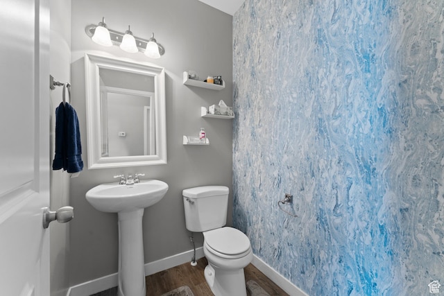 half bath featuring toilet, wood finished floors, a sink, and baseboards