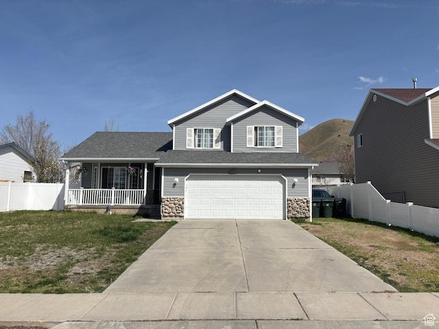 split level home featuring concrete driveway, stone siding, fence, and an attached garage