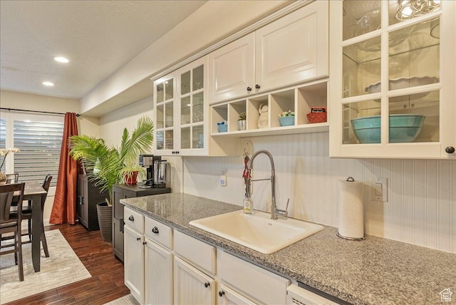 kitchen featuring glass insert cabinets, open shelves, white cabinetry, a sink, and dark wood-style floors