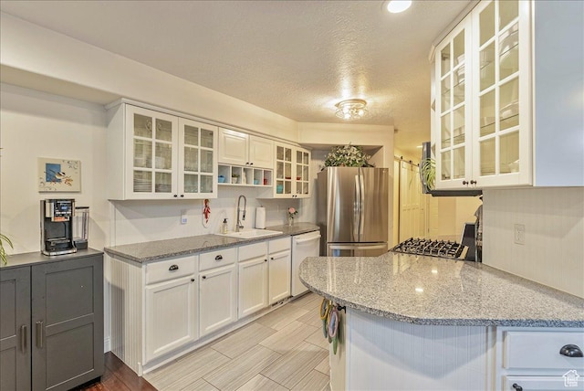 kitchen featuring light stone counters, freestanding refrigerator, white cabinets, white dishwasher, and a sink