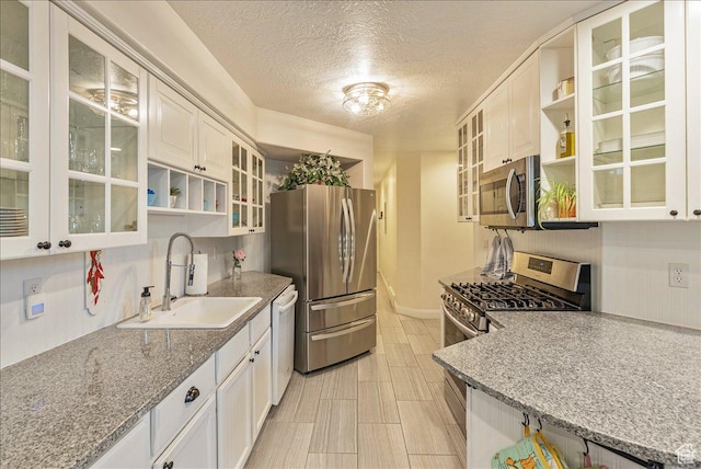 kitchen featuring a textured ceiling, open shelves, light stone countertops, stainless steel appliances, and a sink