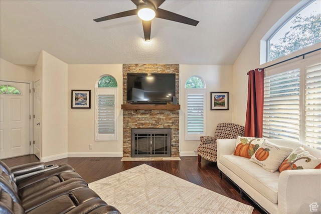 living area with a ceiling fan, vaulted ceiling, a stone fireplace, baseboards, and hardwood / wood-style flooring