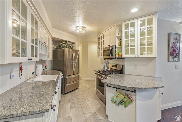 kitchen featuring open shelves, a sink, a textured ceiling, wood finish floors, and stainless steel appliances