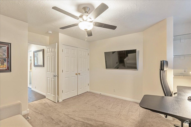 carpeted office space featuring baseboards, a ceiling fan, and a textured ceiling