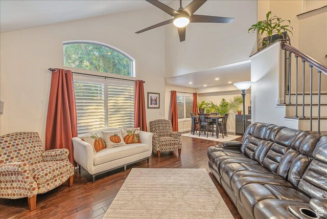 living area featuring stairway, a ceiling fan, a towering ceiling, and dark wood-style floors