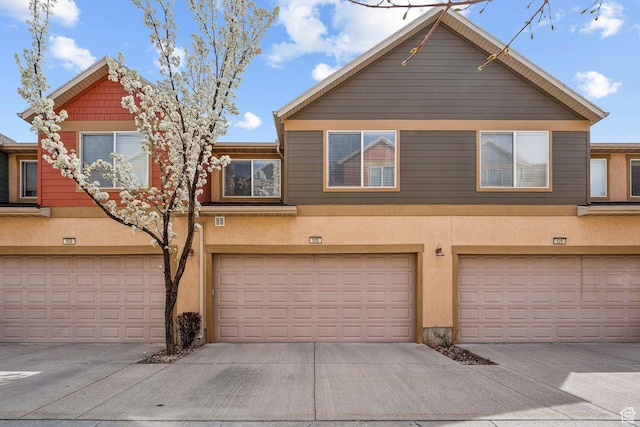 multi unit property with an attached garage, driveway, and stucco siding