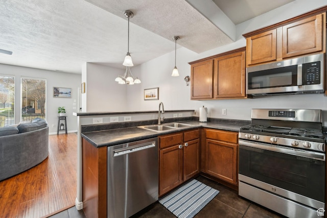 kitchen with a peninsula, dark countertops, a sink, and stainless steel appliances