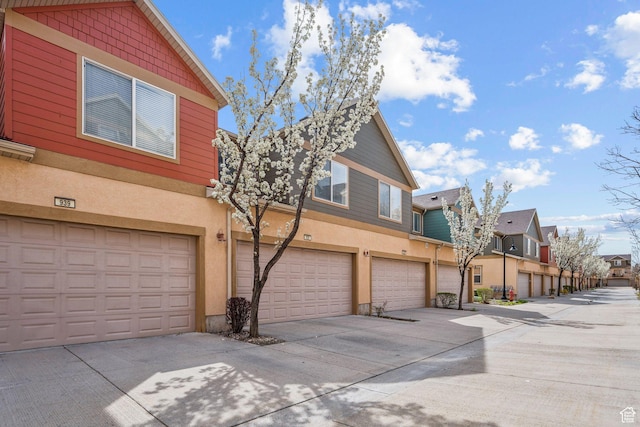 view of front of house featuring driveway, a residential view, a garage, and stucco siding