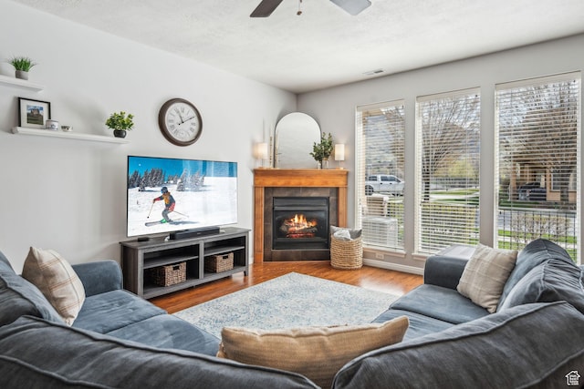 living area featuring a tiled fireplace, visible vents, a ceiling fan, and wood finished floors