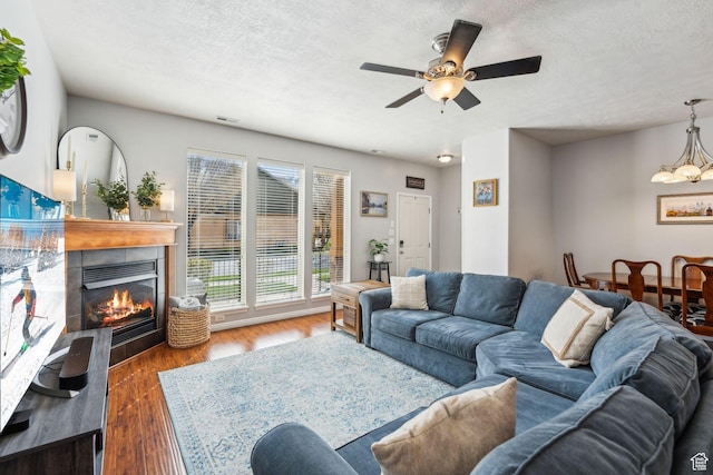 living room with ceiling fan with notable chandelier, a tile fireplace, wood finished floors, and a textured ceiling