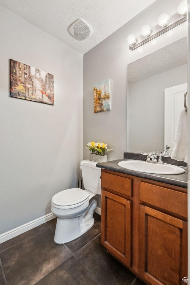 half bath with baseboards, toilet, a textured ceiling, vanity, and tile patterned flooring