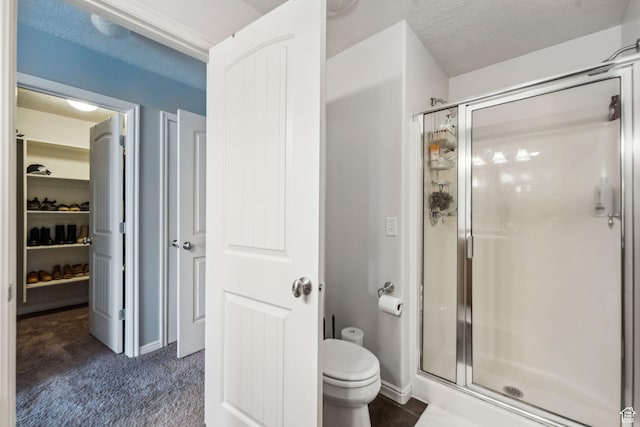 full bathroom with a shower stall, a textured ceiling, a walk in closet, and toilet