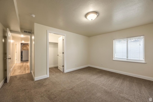 unfurnished bedroom featuring carpet, baseboards, a walk in closet, a textured ceiling, and a closet